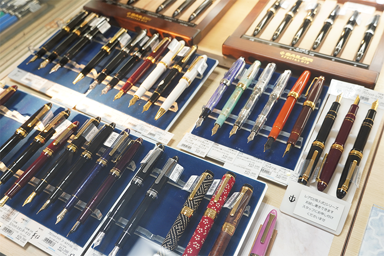 Les stylos-plumes alignés dans la vitrine sont disponibles dans une variété de couleurs, de formes et de largeurs de plume.