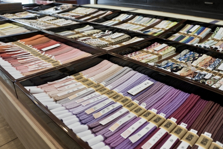 Les ceintures obi sont alignées dans un espace restreint. Les cordons, teints et tissés à la main, créent un dégradé vibrant.