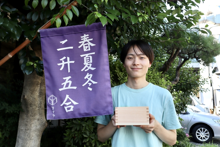 Hayato Oguchi du service des ventes. Le drapeau représente « les affaires (sans automne), la croissance (deux tasses à mesurer) et la prospérité (une demi-tasse à mesurer) ».