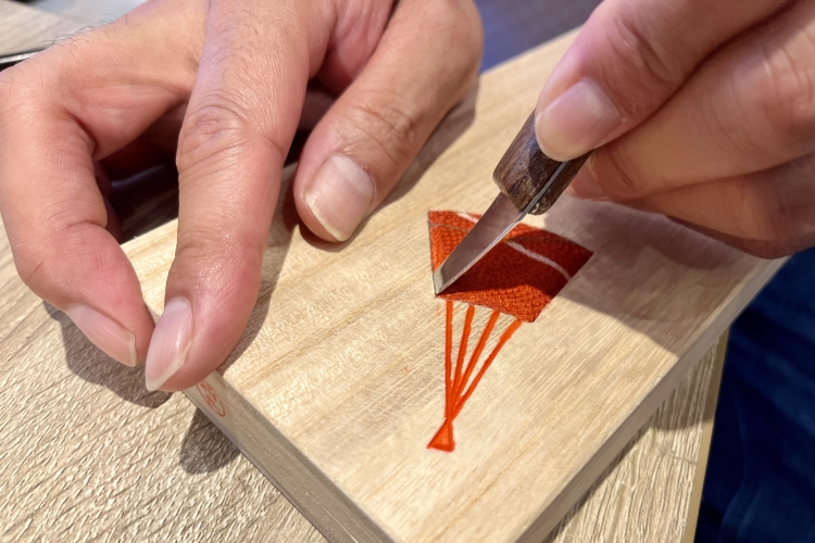 Dans l'artisanat "Kiri-mokumekomi" (incrustation de bois de paulownia), le bord du tissu est pressé dans les rainures sculptées avec un couteau à sculpter à l'aide d'une spatule.